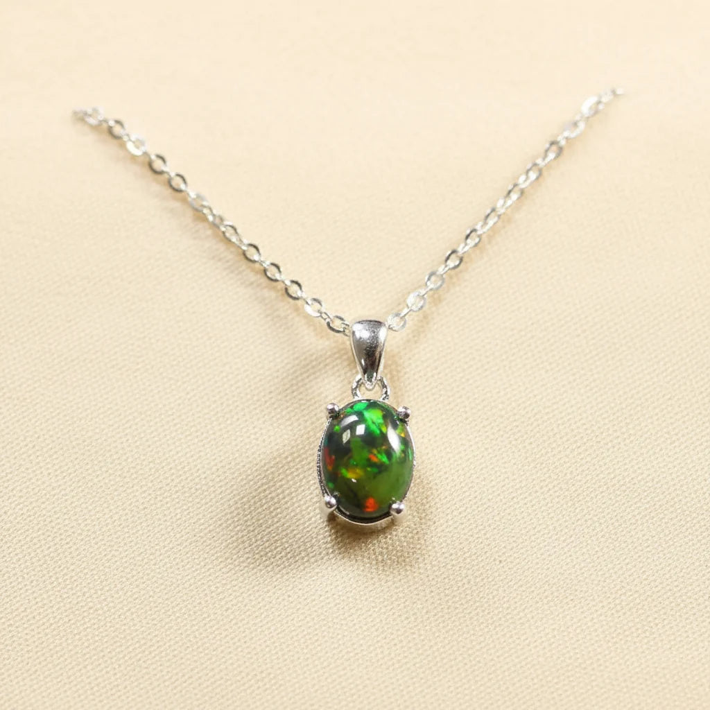 A silver chain necklace with an oval green opal pendant, displayed on a textured cream fabric texture background 