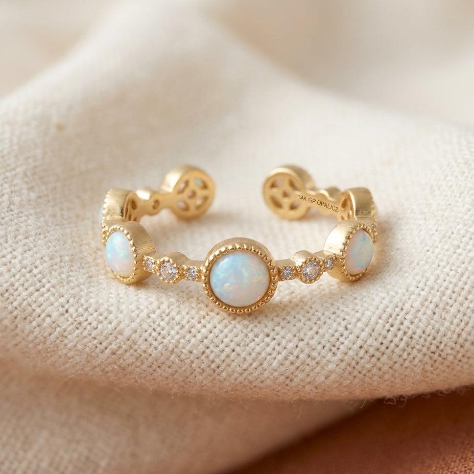 Adjustable gold-tone band with white opal cabochon stations and beaded milgrain edges on cream textile