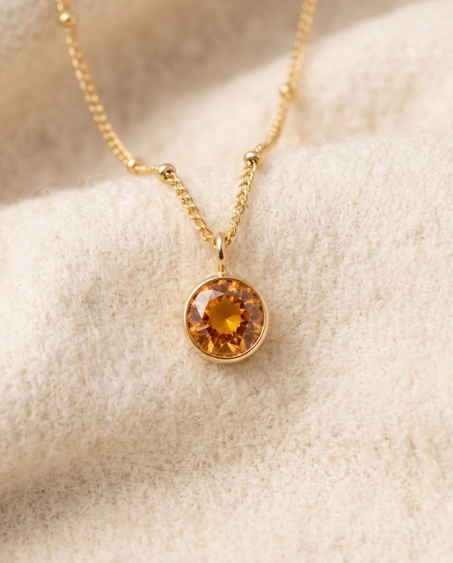 By Sophi Personalized Amber Birthstone Pendant Necklace flat-lay on warm cream wool