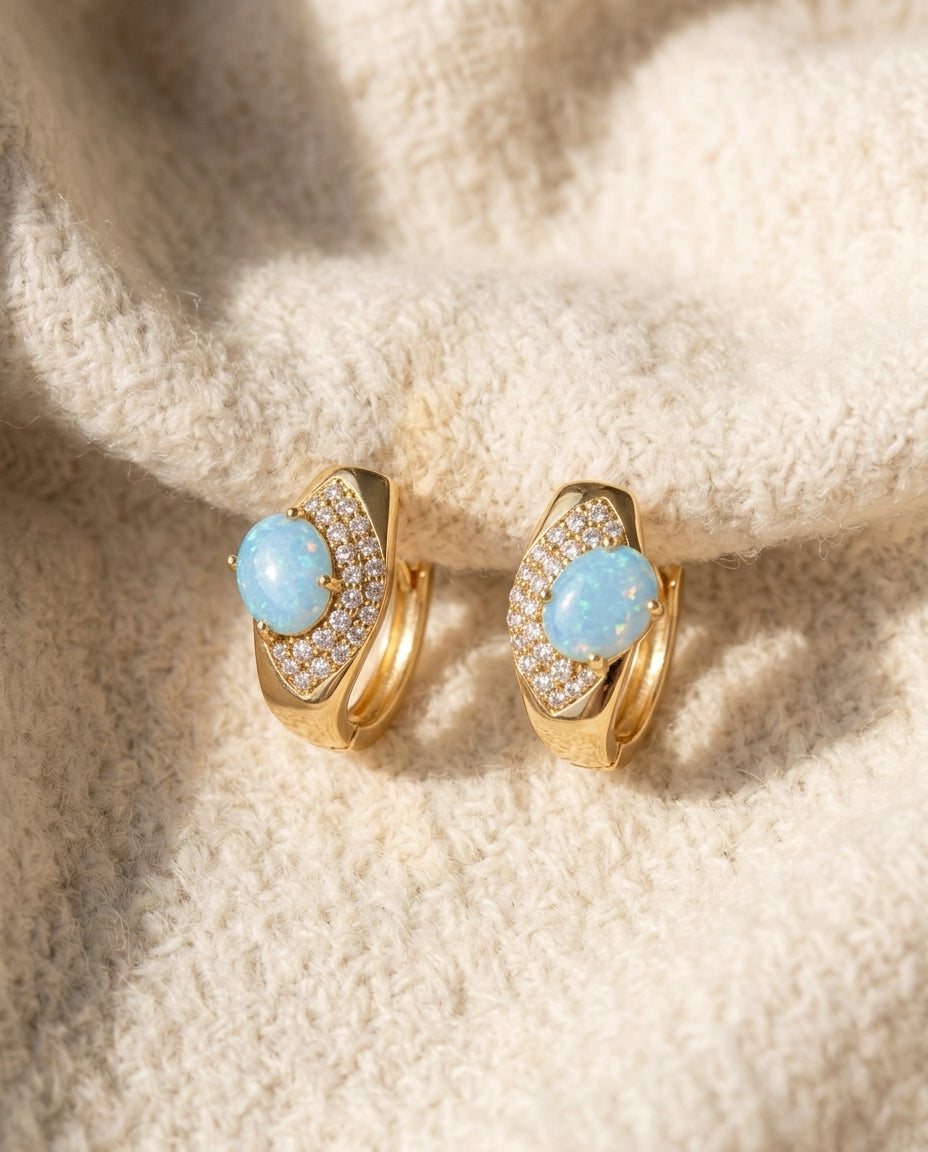 By Sophi Blue Opal Huggie Earrings flat-lay on warm cream wool