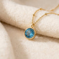 By Sophi Blue Topaz Birthstone Pendant Necklace flat-lay on warm cream wool