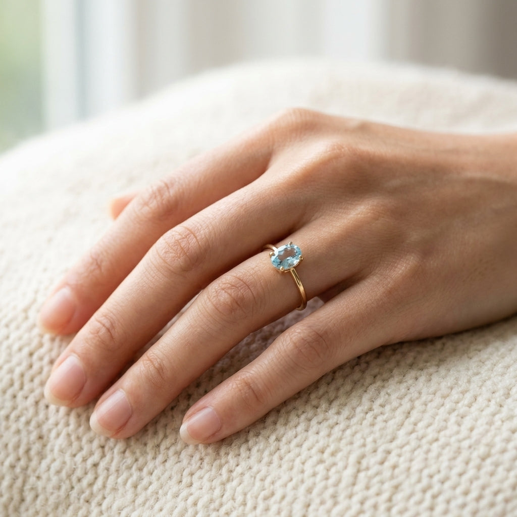 By Sophi Natural Blue Topaz Solitaire Ring in Gold, worn on hand in soft daylight