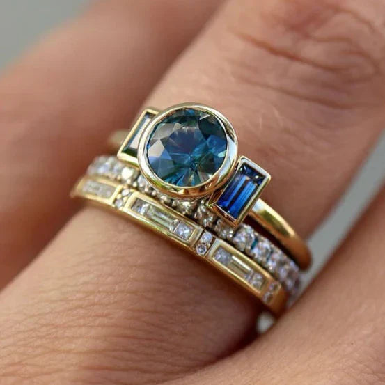 Close-up of a hand wearing three gold rings with gemstones on a neutral background
