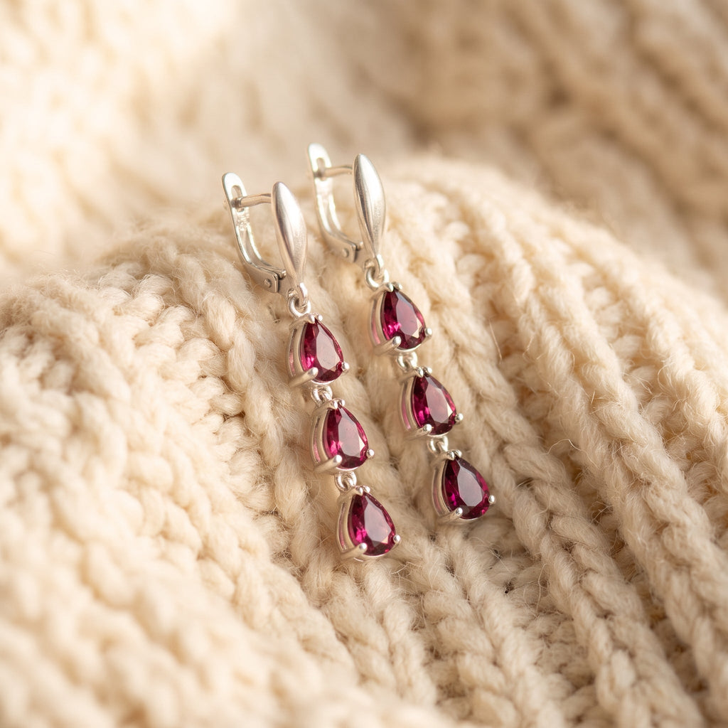 By Sophi Natural Rhodolite Garnet Drop Earrings, catalog flat-lay on warm cream wool