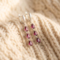 By Sophi Natural Rhodolite Garnet Drop Earrings, catalog flat-lay on warm cream wool