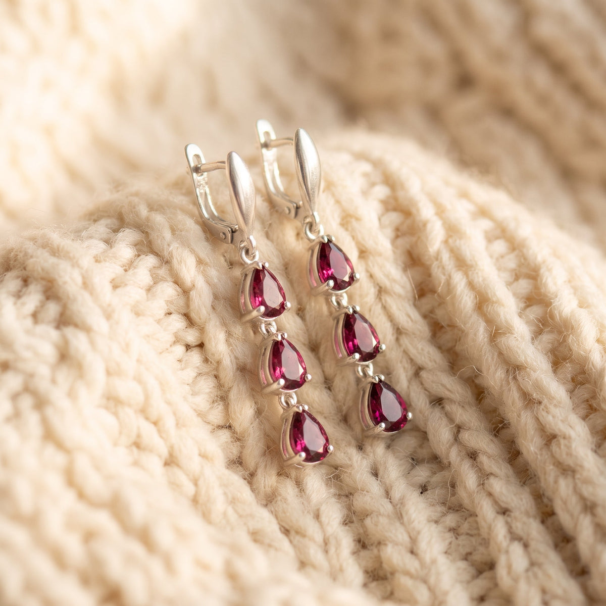 By Sophi Natural Rhodolite Garnet Drop Earrings, catalog flat-lay on warm cream wool