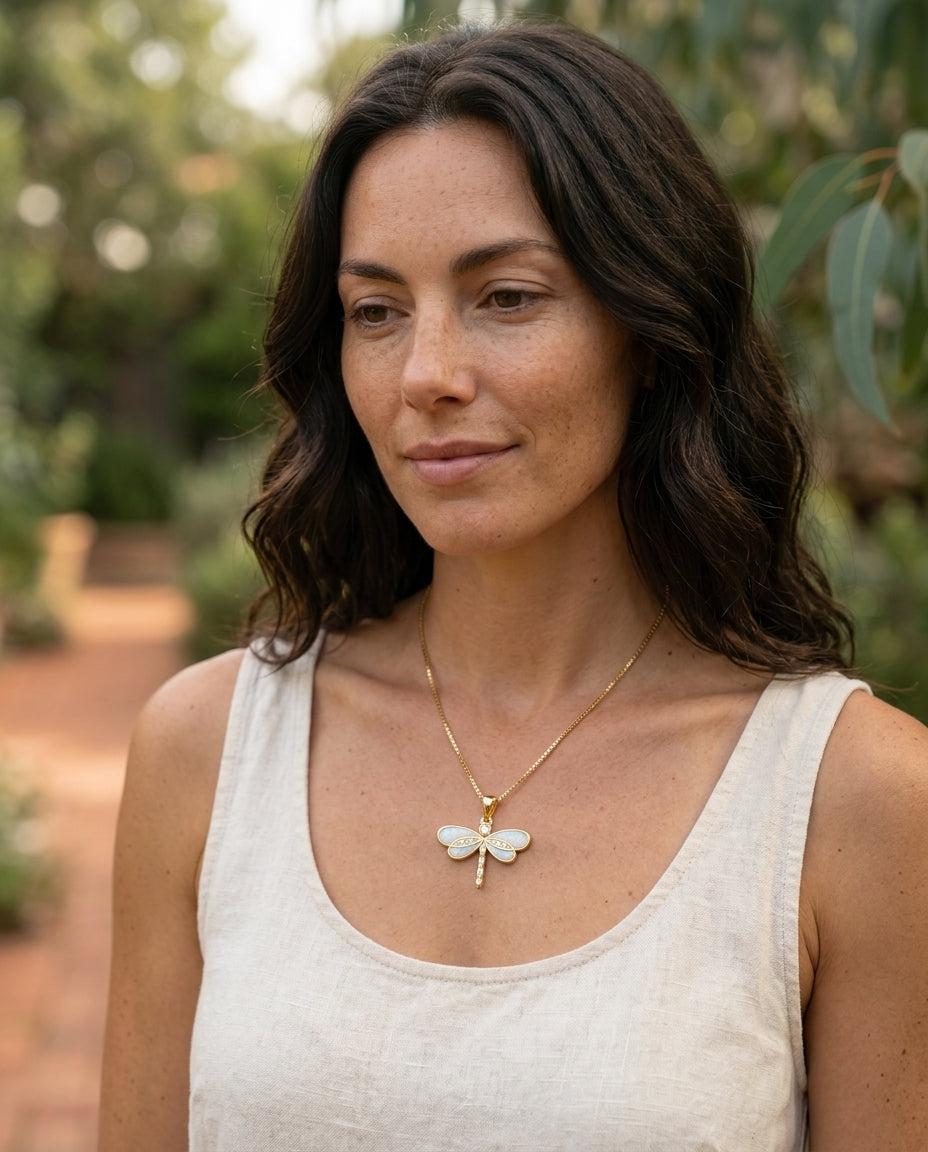 Dragonfly Necklace in gold with opal worn at collarbone, natural daylight, cream linen
