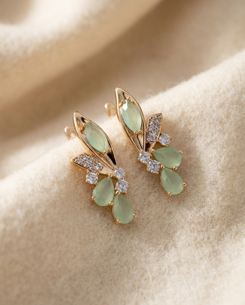 By Sophi Elegant Green Wings Crystal Earrings flat-lay on warm cream wool