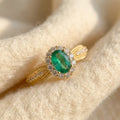 By Sophi Natural Emerald Halo Ring, catalog flat-lay on warm cream wool