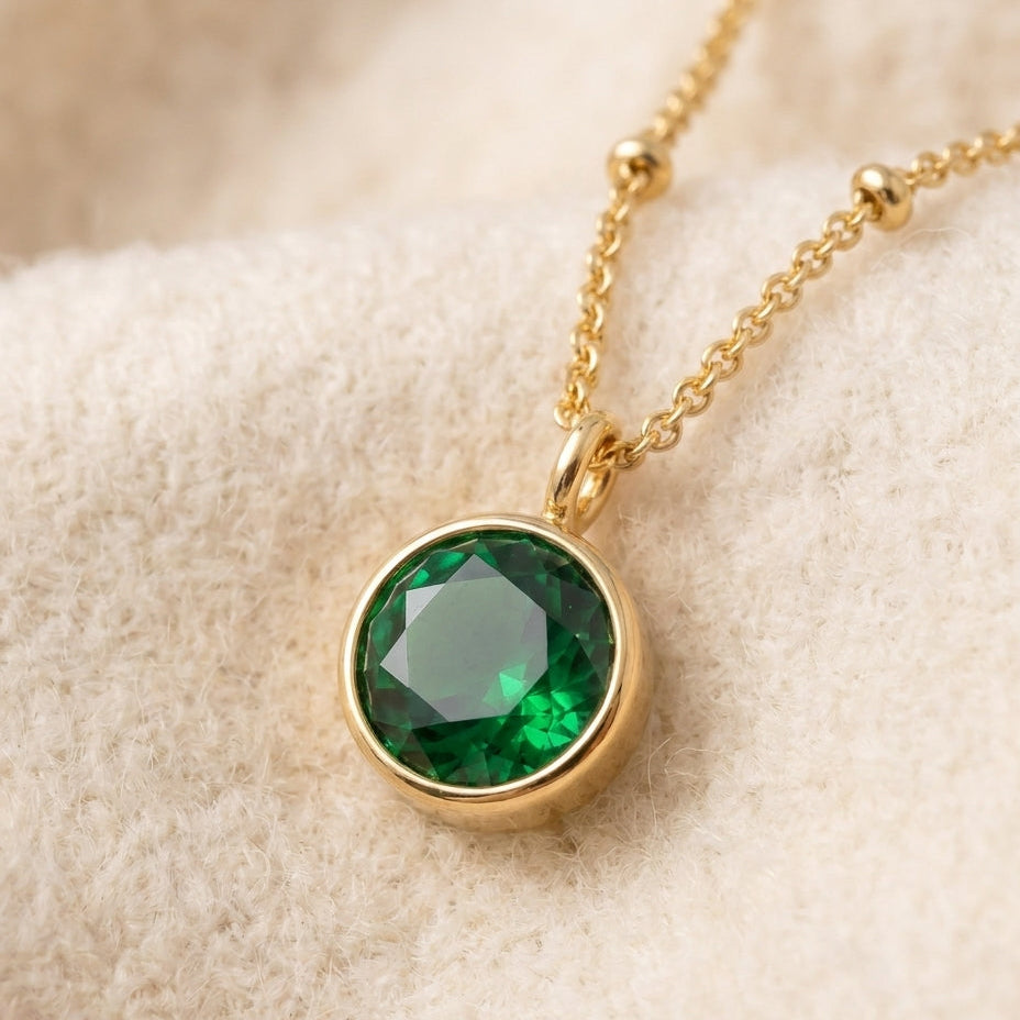 By Sophi Emerald Birthstone Pendant Necklace flat-lay on warm cream wool