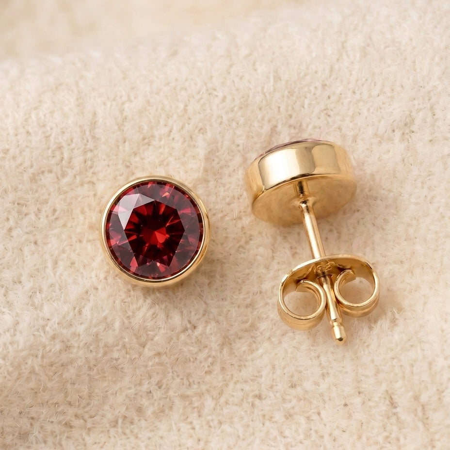 By Sophi Garnet Birthstone Studs flat-lay on warm cream wool
