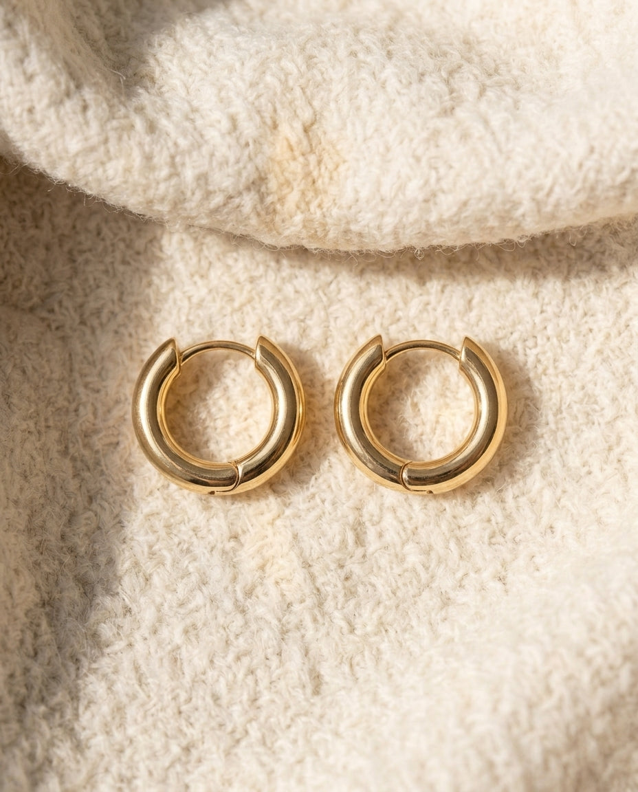 By Sophi Minimalist Gold Huggie Hoop Earrings flat-lay on warm cream wool