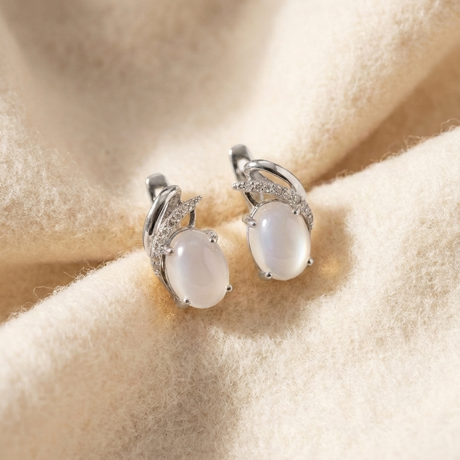 By Sophi Natural White Moonstone Huggie Earrings, catalog flat-lay on warm cream wool