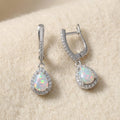 Natural pear-cut opal drop earrings in sterling silver on warm cream wool