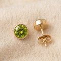By Sophi Peridot Birthstone Studs flat-lay on warm cream wool