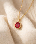 By Sophi Personalized Ruby Birthstone Pendant Necklace flat-lay on warm cream wool