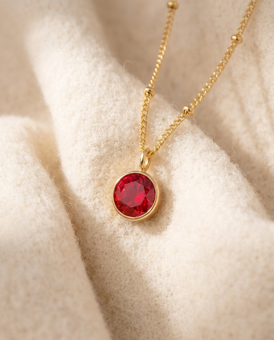 By Sophi Personalized Ruby Birthstone Pendant Necklace flat-lay on warm cream wool