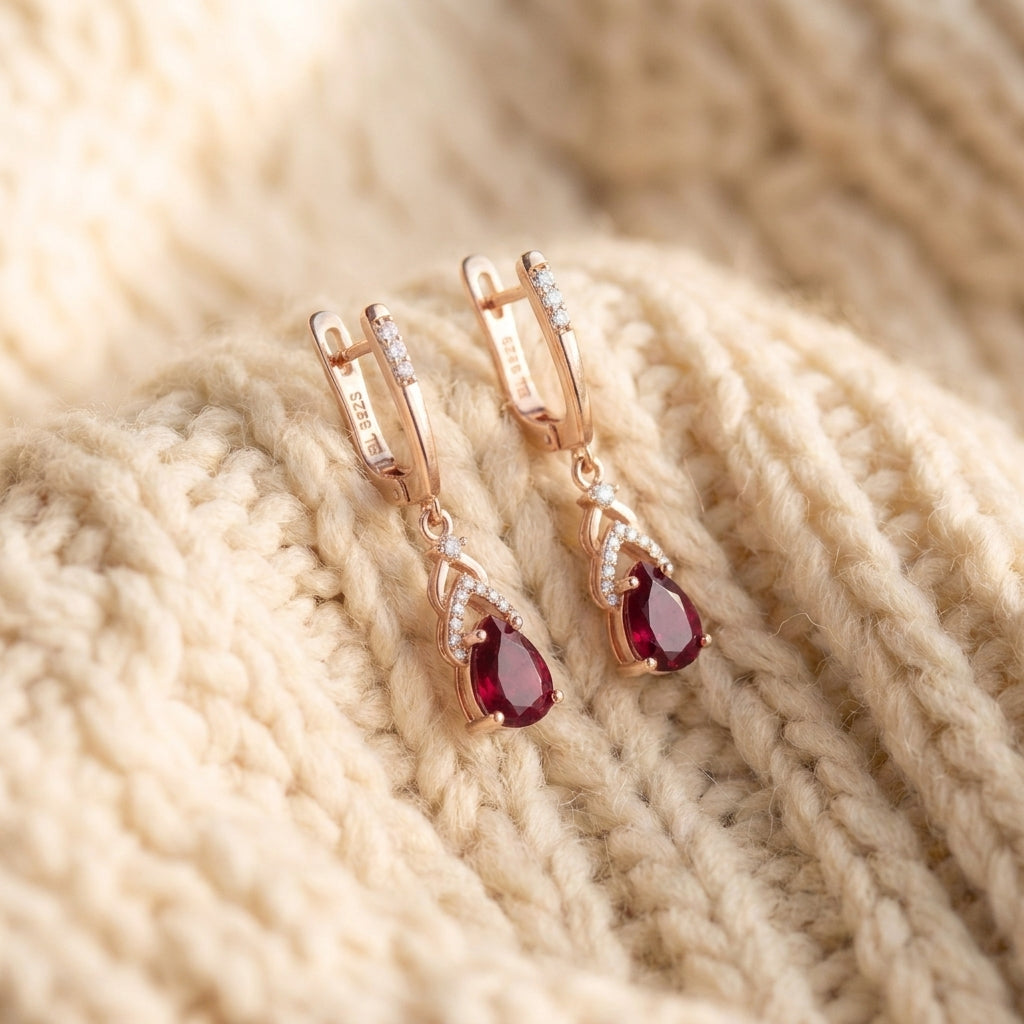 By Sophi Composite Ruby Pear Drop Earrings, flat-lay on warm cream wool