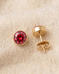 By Sophi Ruby Birthstone Studs flat-lay on warm cream wool