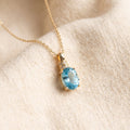 Sky blue topaz pendant necklace, yellow gold chain and bail, on warm cream wool
