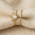 Vintage solar opal ring set on cream textile, two gold-tone rings with sunburst pattern and white opal center