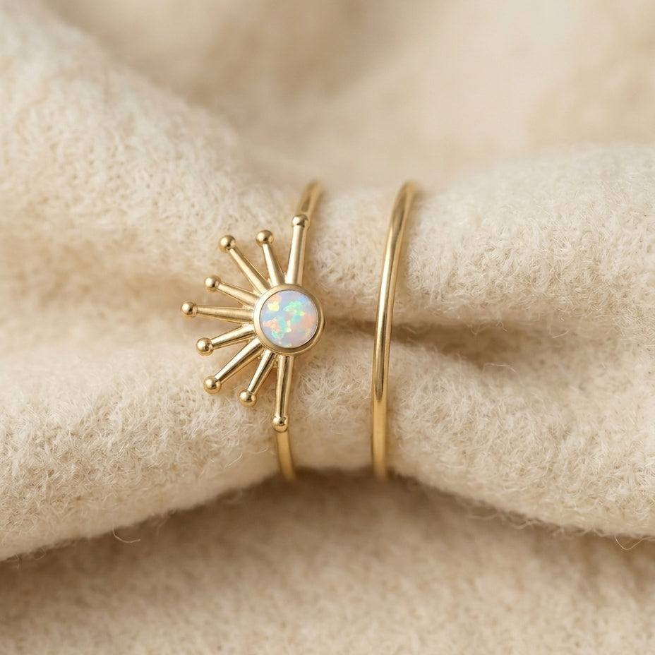 Vintage solar opal ring set on cream textile, two gold-tone rings with sunburst pattern and white opal center