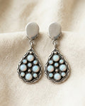 Vintage white opal teardrop drop earrings on cream textile, silver-tone frames with opal cluster inlays