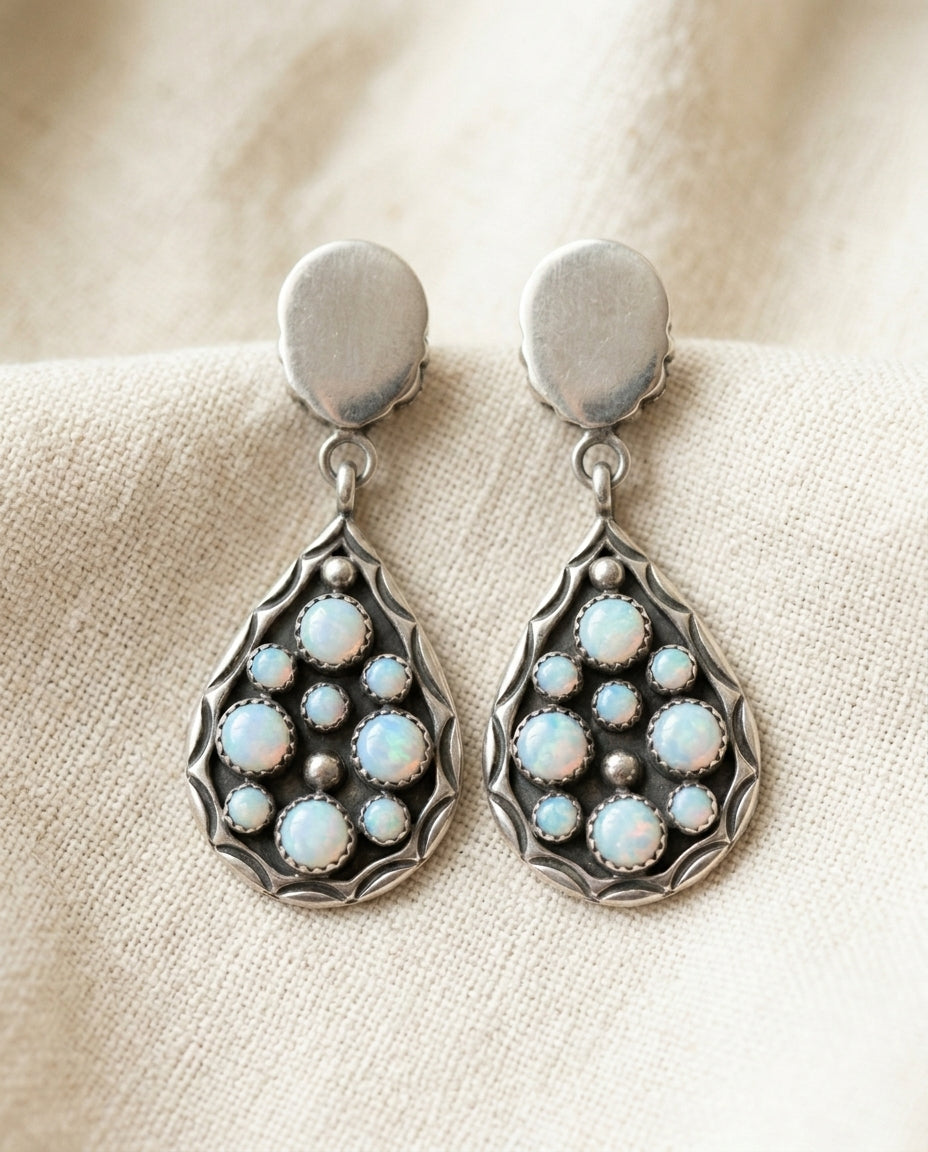 Vintage white opal teardrop drop earrings on cream textile, silver-tone frames with opal cluster inlays