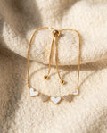 By Sophi White Enamel & Gold Heart Bracelet flat-lay on warm cream wool