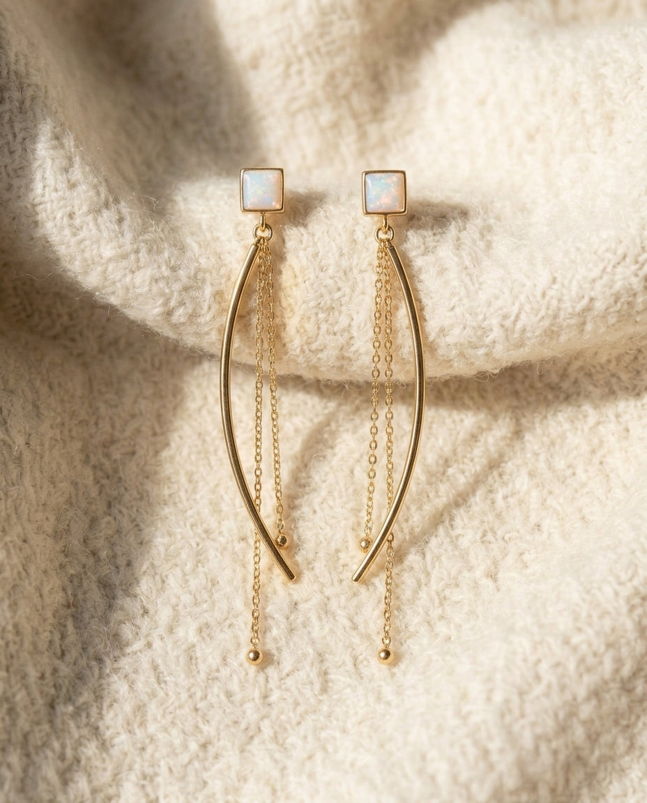 By Sophi White Opal Drop Earrings in Gold flat-lay on warm cream wool