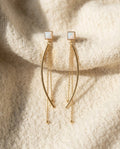 By Sophi White Opal Drop Earrings in Gold flat-lay on warm cream wool