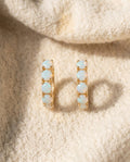 By Sophi White Opal Gold Huggie Earrings flat-lay on warm cream wool